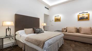 A hotel room with a bed, bedside tables, a sofa, and artwork on the walls.