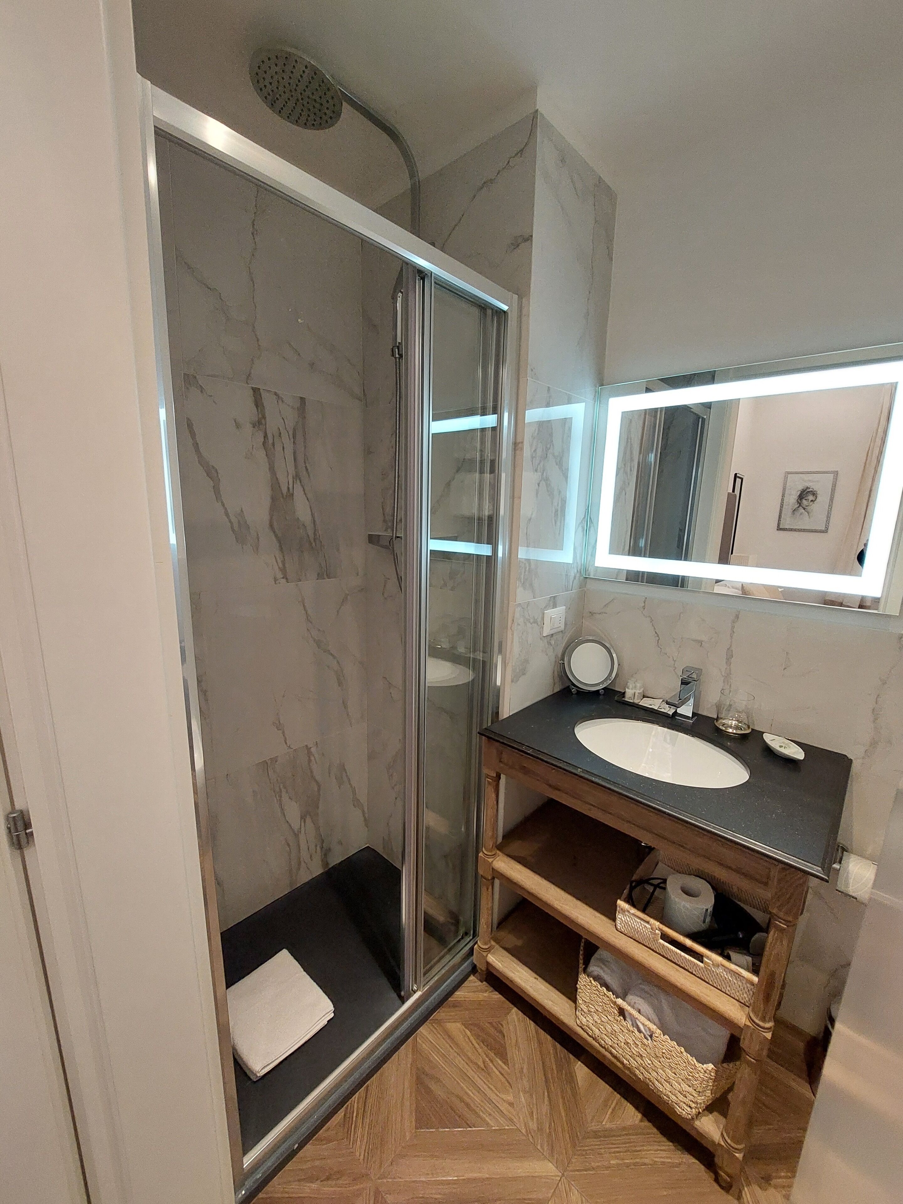 Une salle de bain moderne dotée d’une douche à parois de verre, d’un sol carrelé en marbre, d’un meuble-lavabo en bois et d’un miroir au-dessus du meuble.