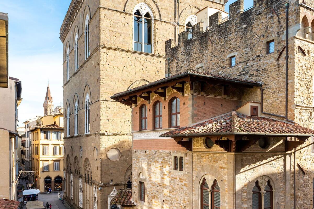 A historic building with arched windows and a tiled roof, located in a narrow street with pedestrians and parked bicycles.