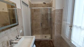 A modern bathroom with a glass shower enclosure, a large mirror, and a vanity with a sink.