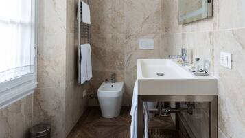 Un baño moderno con suelo de mármol, un lavabo blanco, un bidé y un espejo sobre el lavabo.