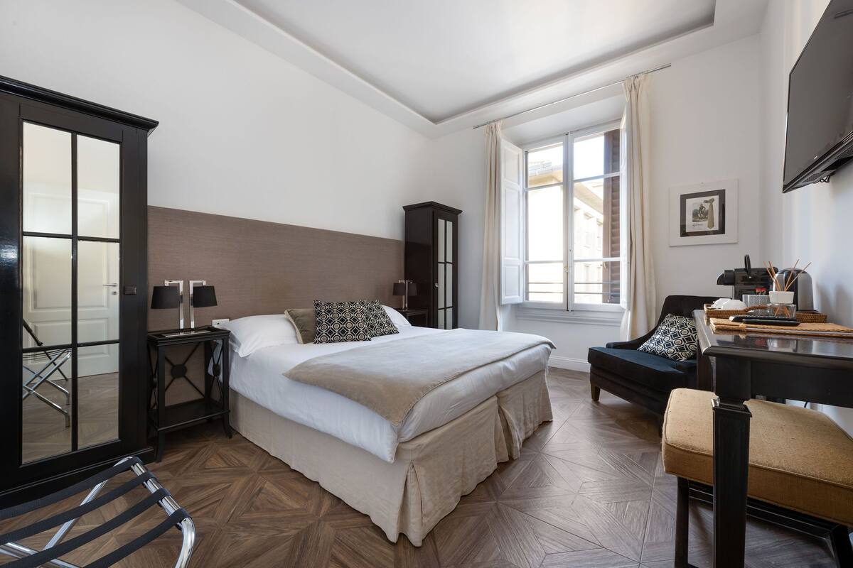 A bedroom with a bed, a desk, a chair, a wardrobe, and a window.