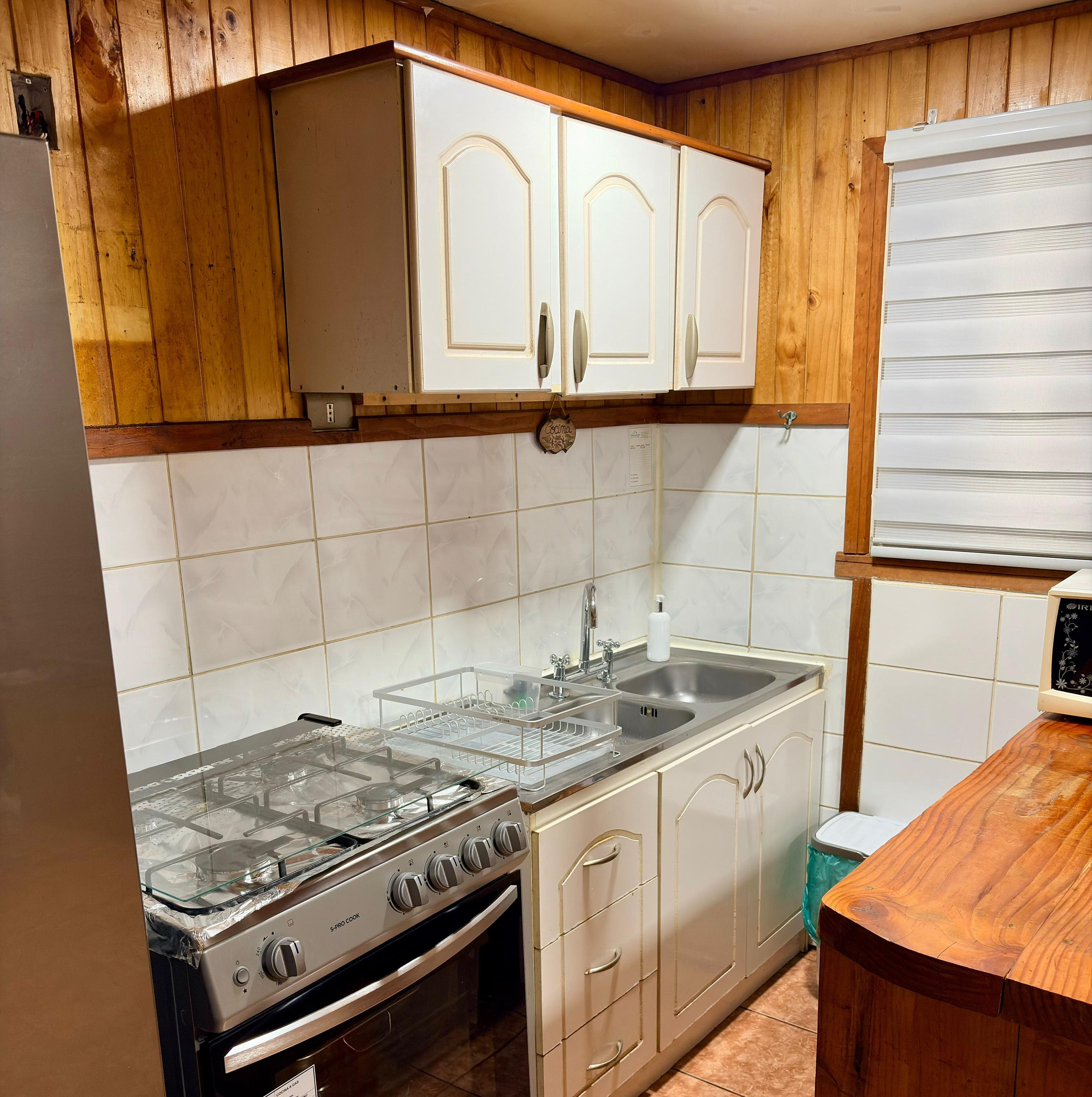Una cocina con armarios de madera, un lavamanos de acero inoxidable y una estufa a gas.