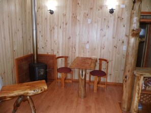 A wooden interior with a table and chairs, a wood-burning stove, and a bench.
