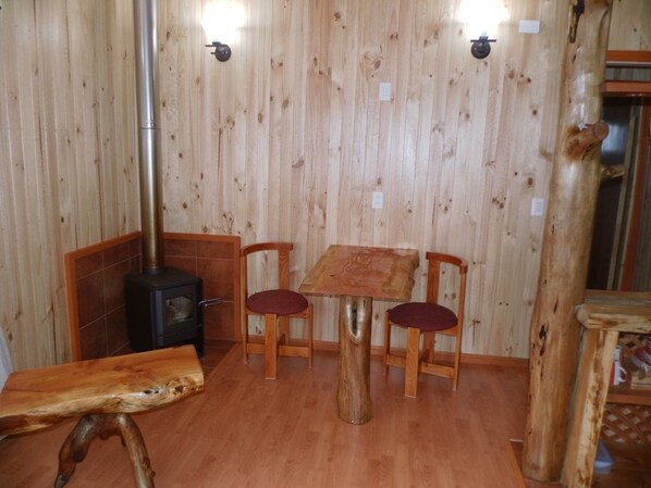 A wooden interior with a table and chairs, a wood-burning stove, and a bench.
