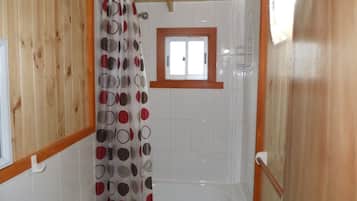 A bathroom with a shower, toilet, and a window above the shower.