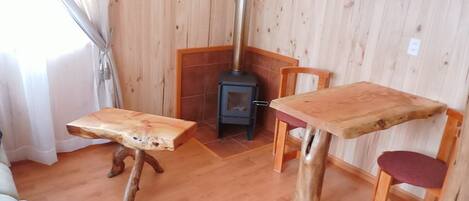 A room with a wooden floor, a table with a unique design, a chair, and a wood-burning stove.
