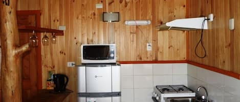 A compact kitchen with wooden walls, a microwave, a refrigerator, a stove, and a sink.