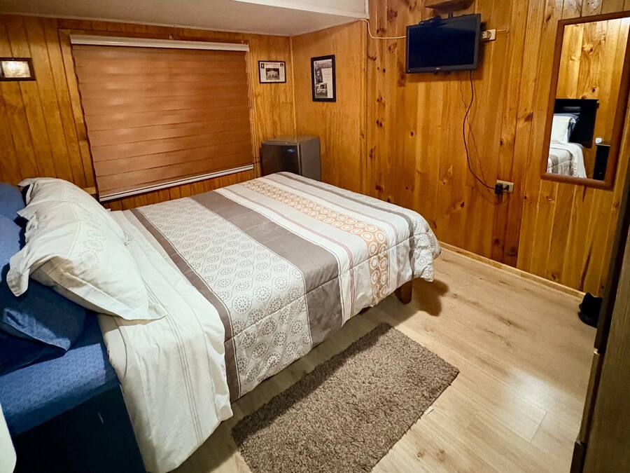 A bedroom with a bed, a television mounted on the wall, and a wooden floor.