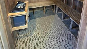 A sauna room with wooden benches and a bench seat, a small table, and a mat on the floor. - Oceanfront Daytona Beach Condo – Magnificent Views, Pools & Beach Access (Daytona Beach)