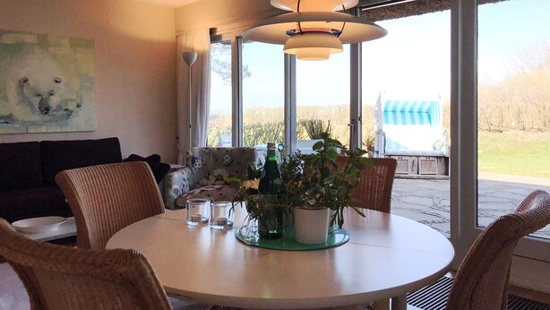 A dining area with a round table, chairs, a potted plant, and a painting on the wall. - Cosy, nicely furnished apartment with spacious sunny terrace (Wenningstedt-Braderup (Sylt))