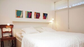 A bedroom with a bed, a bedside table, a lamp, and abstract wall art. - Cosy, nicely furnished apartment with spacious sunny terrace (Wenningstedt-Braderup (Sylt))