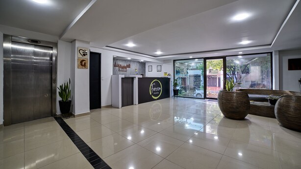 A modern hotel lobby with a reception desk, a reception area, a seating area, and a large window offering a view of the outdoors. - Farum Hotel Medellin (Medellín)