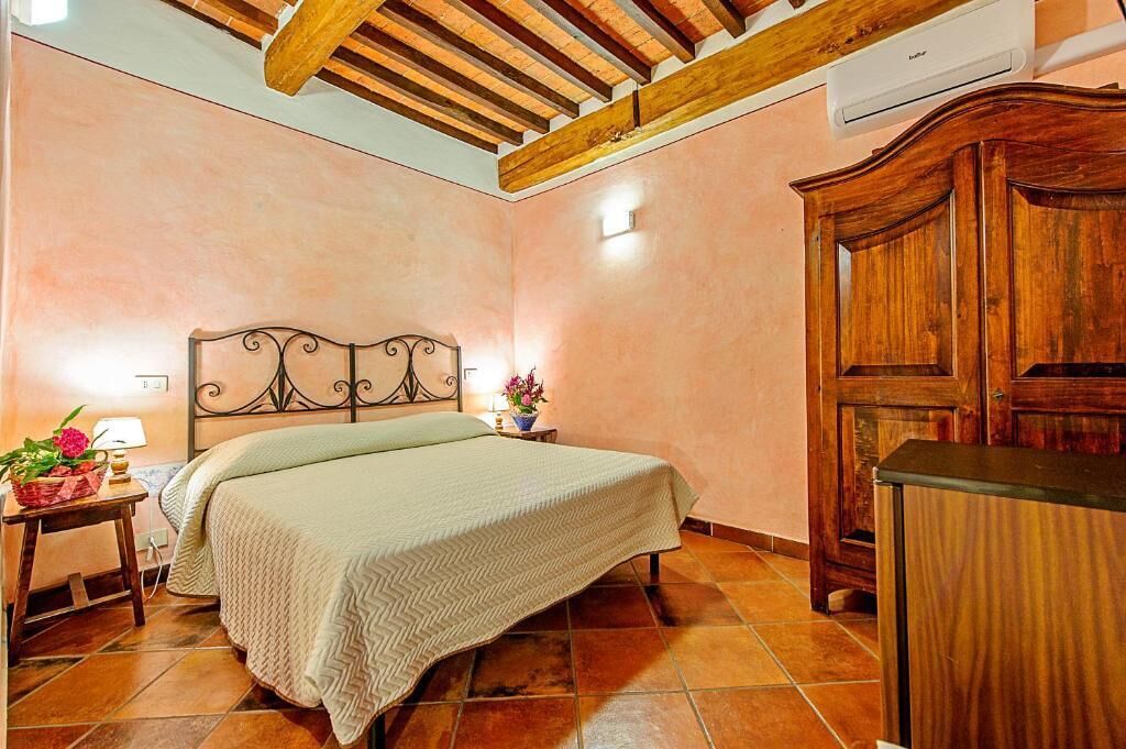 A bedroom with a bed, wooden wardrobe, and a nightstand with a lamp and flowers.