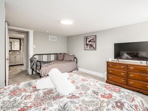 Une chambre à coucher avec un lit, une commode, une télévision et une salle de bain visible à travers une porte ouverte.