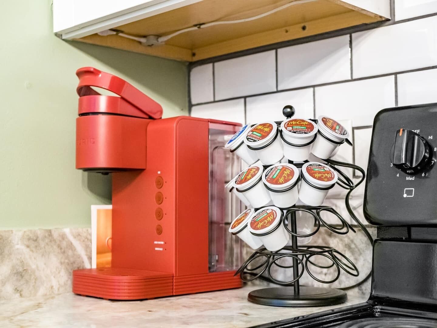 A red coffee maker and a coffee dispenser with multiple cups on a kitchen counter.