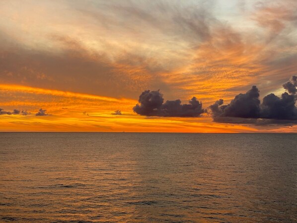 Een zonsondergang boven een rustige zee met wolken aan de lucht.