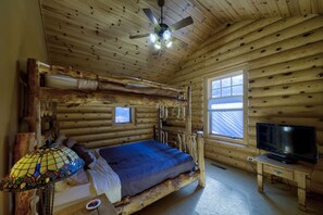 A log cabin room with a bed, a television, and a small window.