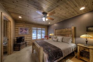A log cabin bedroom with a bed, a television, and a ceiling fan.