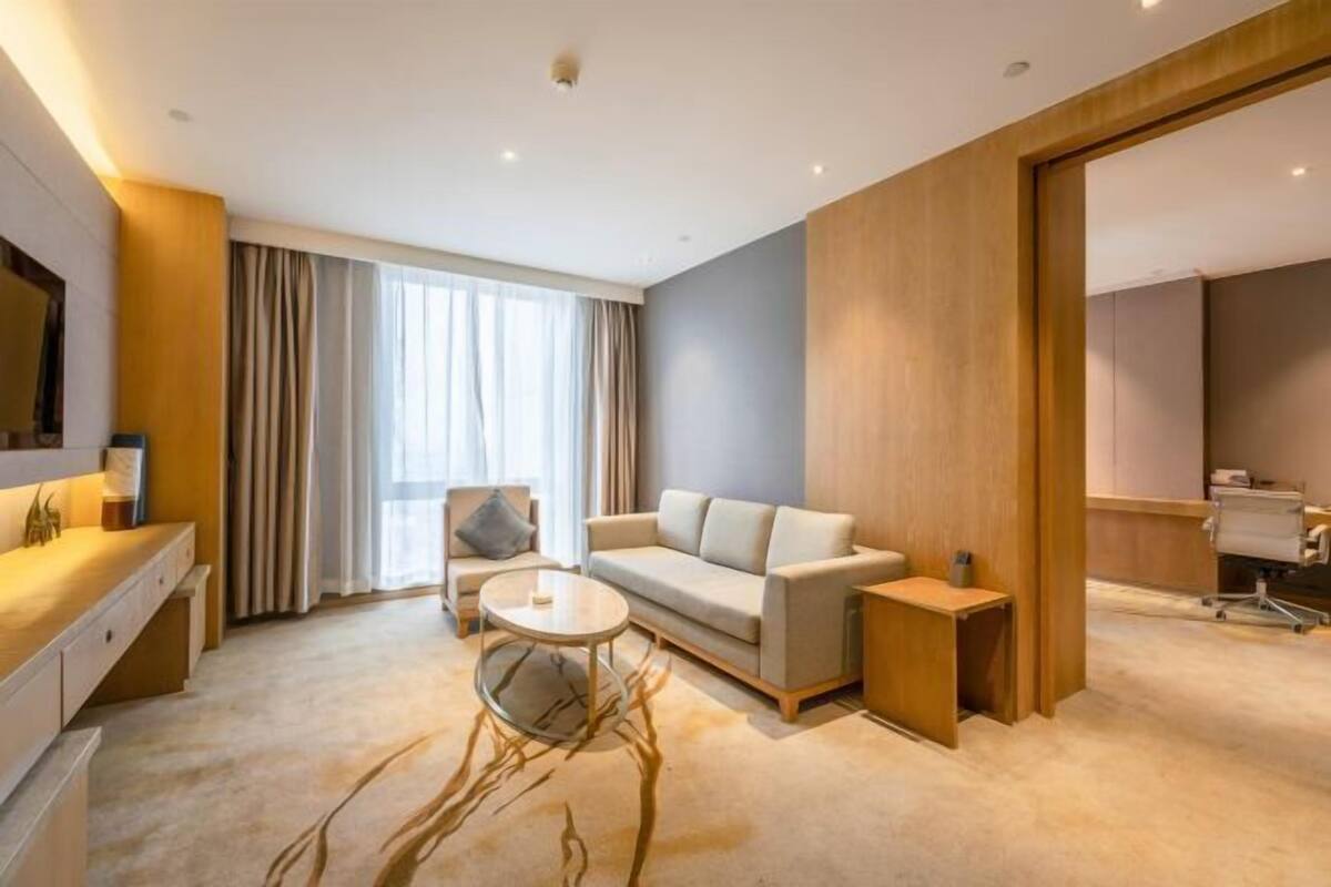 Quarto de hotel moderno com sofá, uma pequena mesa redonda, escrivaninha e um espelho grande.