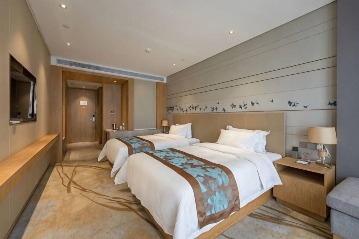 Quarto de hotel com duas camas, uma escrivaninha, uma cadeira, uma televisão e uma parede decorada.
