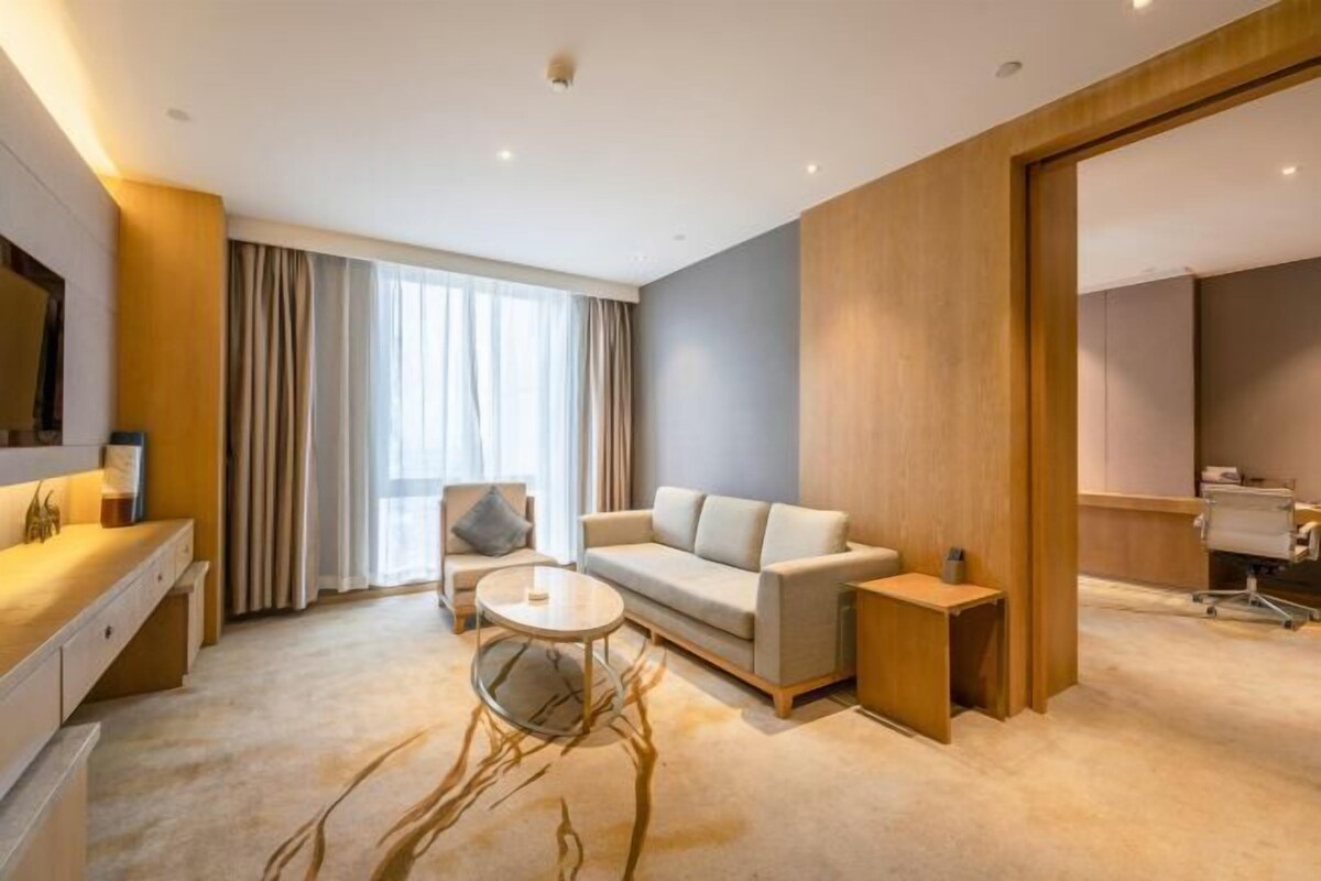 A modern hotel room with a sofa, a small round table, a desk, and a large mirror.