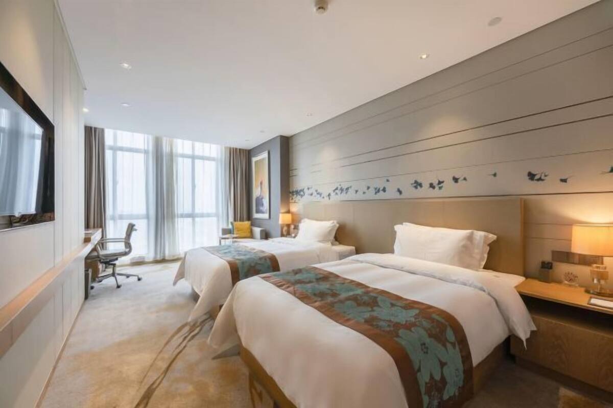 Quarto de hotel com duas camas, uma escrivaninha e uma cadeira.
