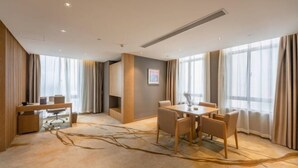 Une chambre d’hôtel moderne dotée d’un coin repas, de grandes fenêtres et d’un tapis au motif naturel.
