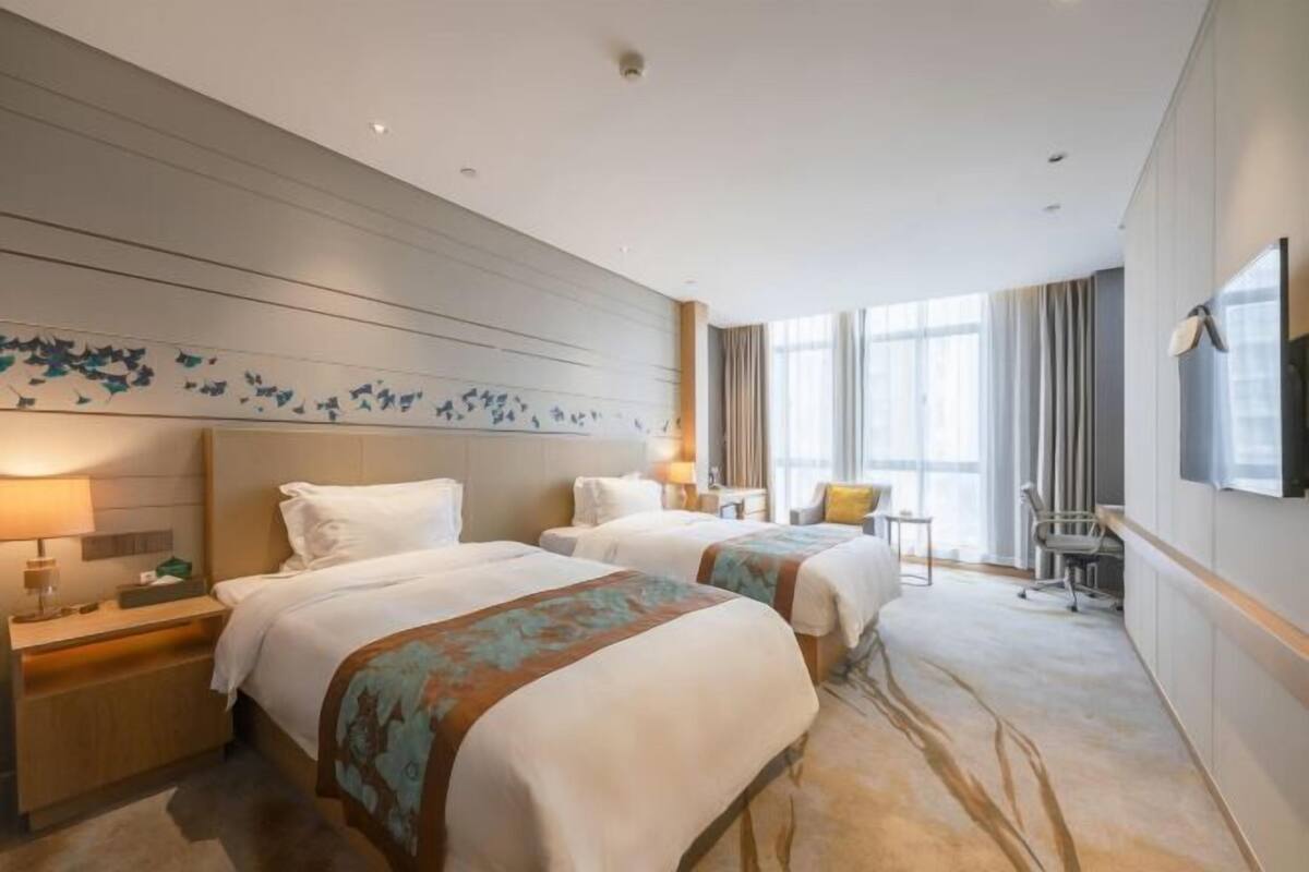 Quarto de hotel com duas camas, uma escrivaninha, uma cadeira e uma televisão.
