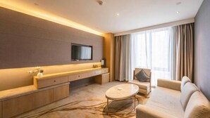 Une chambre d’hôtel moderne, dotée d’un canapé, d’une table basse, d’un téléviseur fixé au mur et d’une grande fenêtre avec des rideaux.