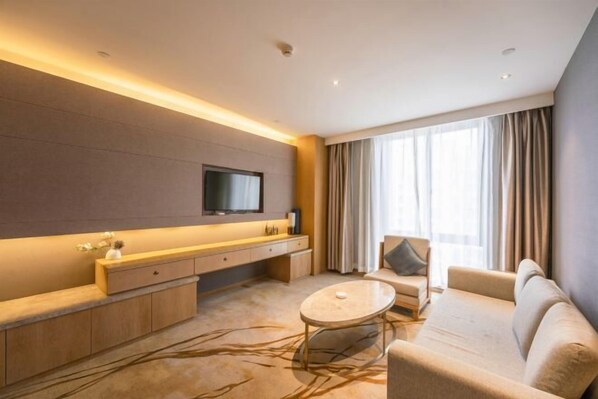 A modern hotel room with a sofa, a coffee table, a TV mounted on the wall, and a large window with curtains. - Qingyang Tongtaiyuan Grand Hotel (Qingyang District) (Qingyang)