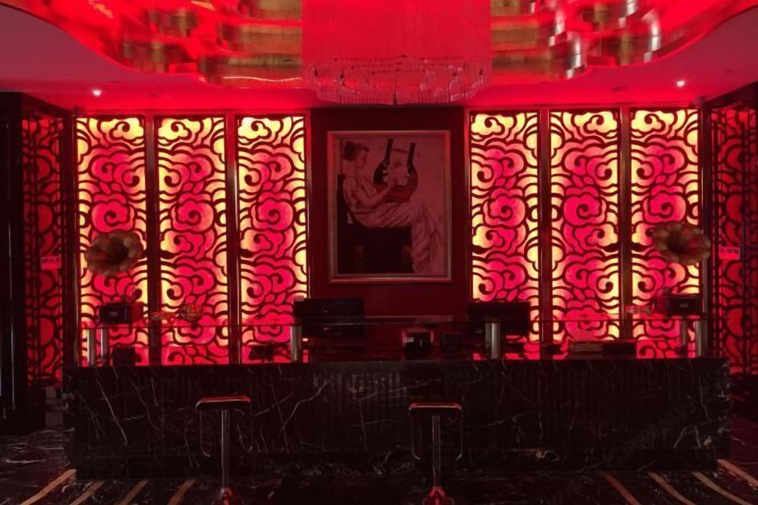 Une pièce faiblement éclairée, avec un fond rouge illuminé, une œuvre d’art encadrée accrochée au mur et un coin bar avec des tabourets.