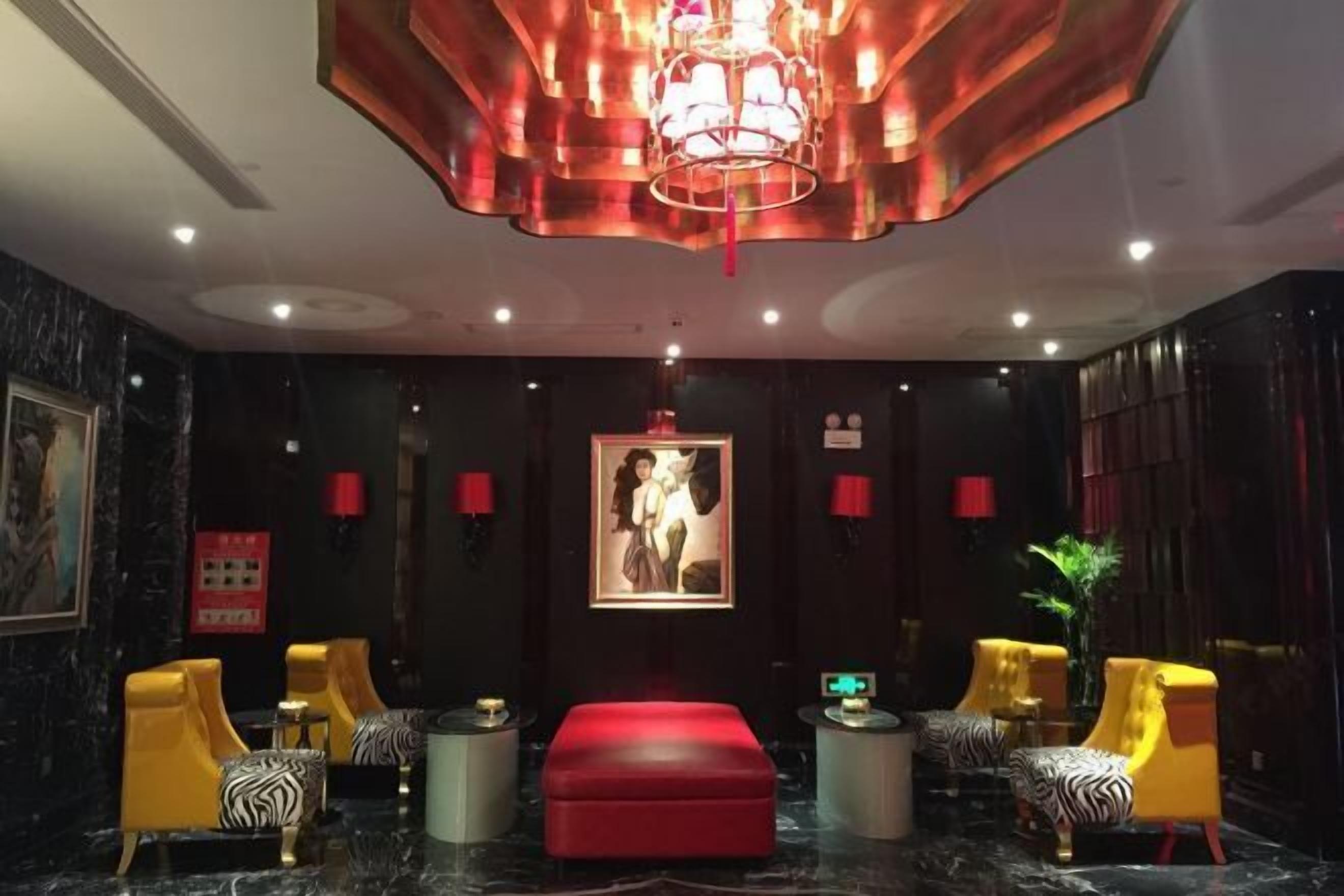 A lobby with a red ottoman, yellow chairs with zebra print cushions, a large framed artwork on the wall, and a modern chandelier.