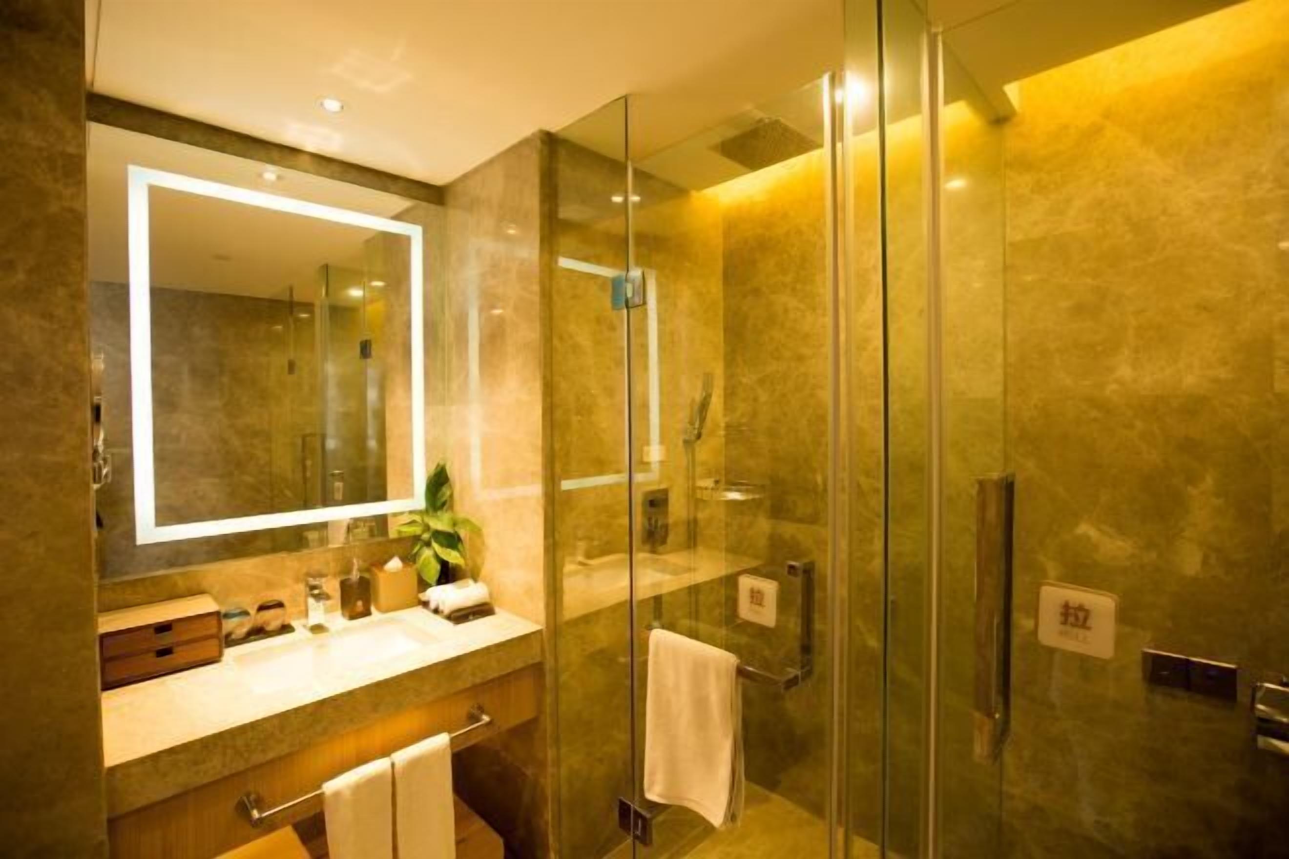 Un baño moderno con ducha de vidrio, un espejo grande y un tocador con una planta.