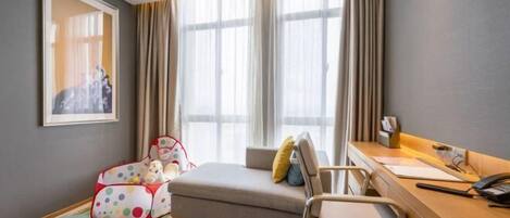 A hotel room with a bed, a desk, a chair, a window with curtains, and a framed picture on the wall.