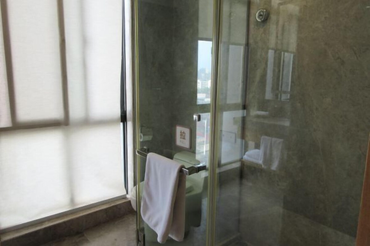 A glass-enclosed shower area with a towel hanging on a rack, a visible bathroom counter, and a reflection of a window and a wall.
