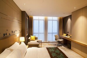 A hotel room with a bed, a desk, a chair, a small table, and a window with curtains. - Qingyang Tongtaiyuan Grand Hotel (Qingyang District) (Qingyang)