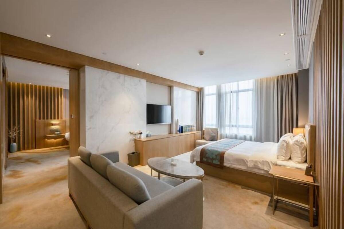 Quarto de hotel moderno com sofá, cama, televisão e escrivaninha.