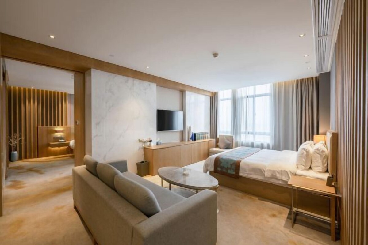 A modern hotel room with a sofa, a bed, a small table, and a TV.