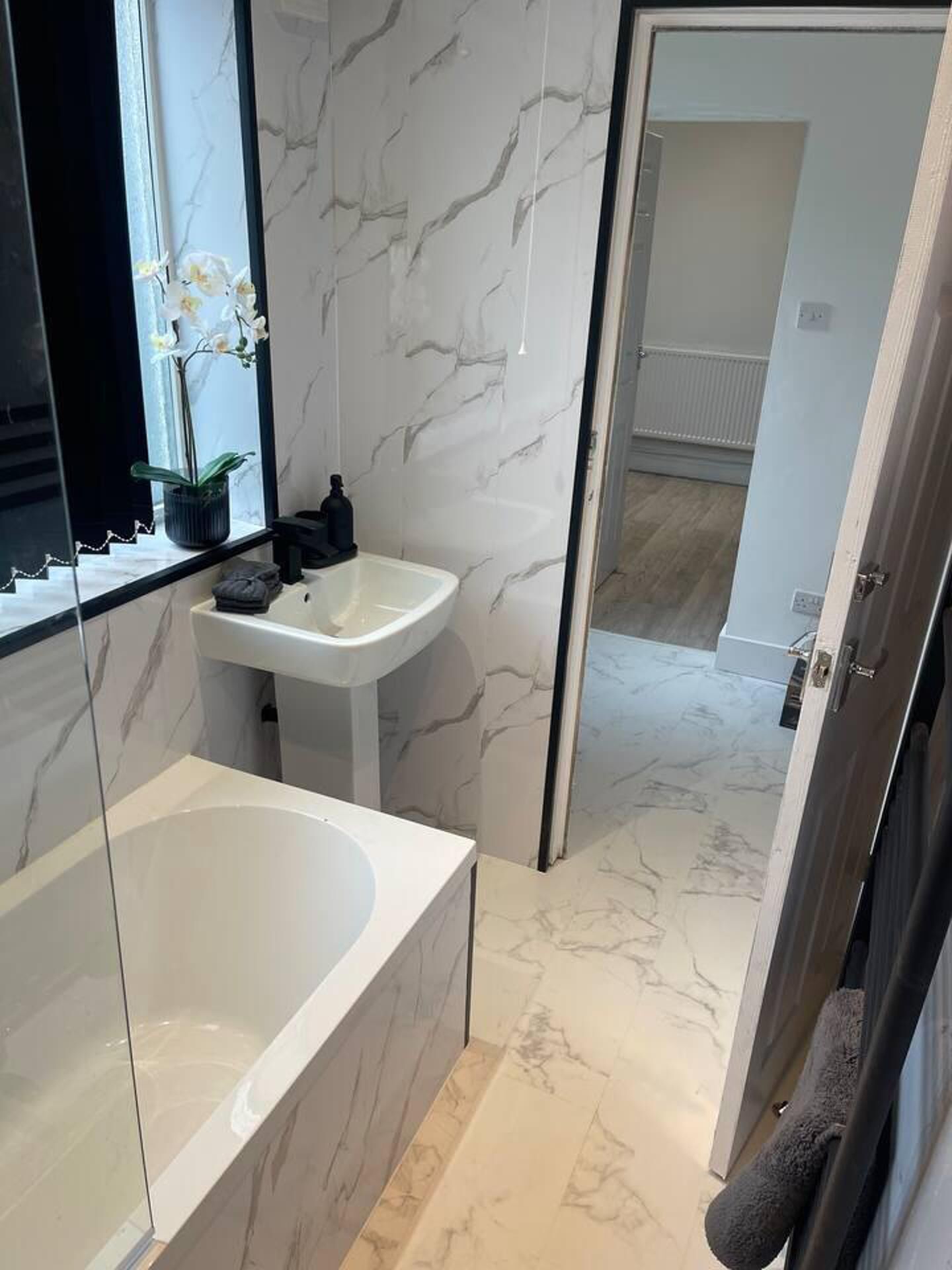 Ein modernes Badezimmer mit Marmorfliesen, einem weißen Waschbecken und einer großen Badewanne.