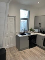 Cocina compacta con lavadora integrada, un lavamanos y una ventana con persianas.