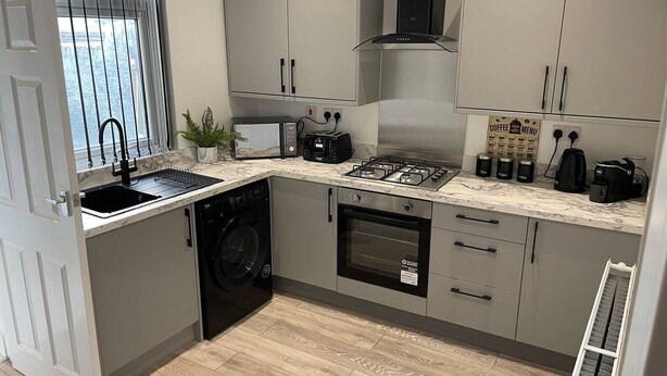 Une cuisine compacte avec des meubles gris, un lave-linge encastré, une cuisinière et une machine à café.