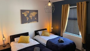 Une chambre d’hôtel avec deux lits, une carte du monde accrochée au mur, un luminaire suspendu et une fenêtre avec des rideaux.