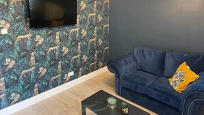 Un salon avec un canapé bleu foncé, un téléviseur à écran plat fixé sur un mur à motifs et un luminaire moderne.