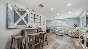 Une pièce spacieuse avec un bar en bois, un canapé blanc et un fauteuil à motifs.