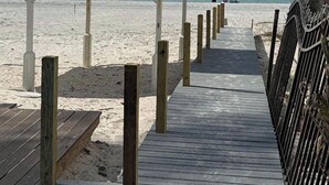 Une promenade en bois mène à une plage où se trouve un kiosque blanc.