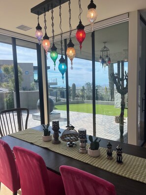 Un coin repas avec une table dressée pour quatre personnes, offrant une vue sur un jardin aménagé et agrémenté d’une sculpture de cactus.