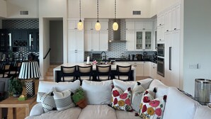 Une cuisine moderne avec des meubles blancs, un coin repas comprenant une table et des chaises, et un salon avec un canapé et des coussins décoratifs.