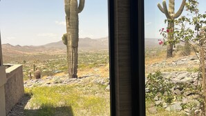 Une vue par la fenêtre sur un paysage désertique, avec des cactus et une ville lointaine.