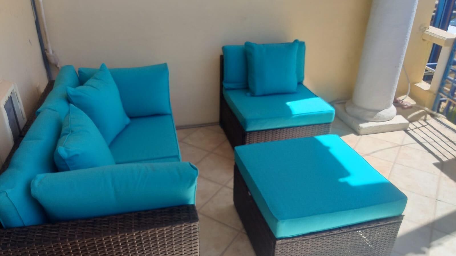 Ein Balkon mit einer Korpus-Sofagarnitur und passendem Hocker, beide mit Stoff in Türkis bezogen.